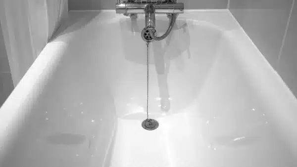 A white bathtub with a chrome faucet and a chain hanging from the drain plug, perfect for easy drain cleaning, set against tiled walls.