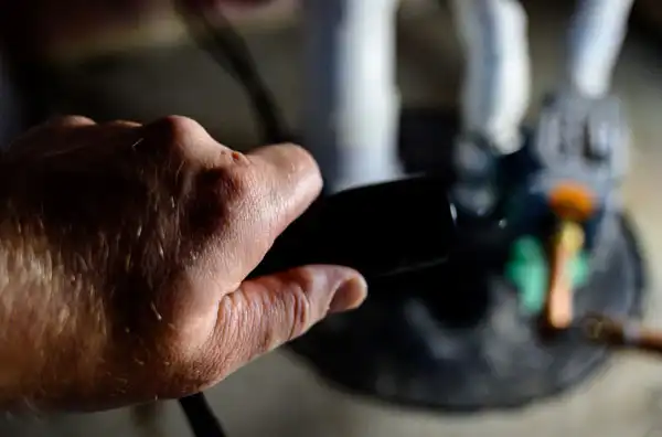 A hand holding a black TV remote control, pointing towards a television screen displaying an out-of-focus scene.